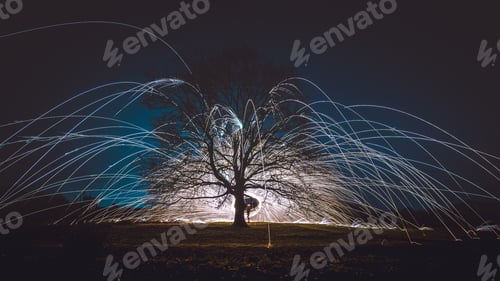 Preview: A Steel Wool Spinning Above The Ground Near A Tree During The Night