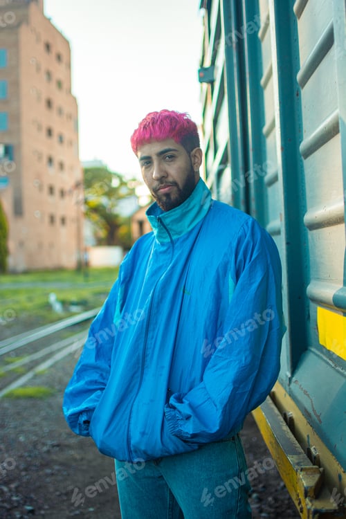 Preview: A Fashionable Young Man With Stylish Pink-Dyed Hair Wearing A Retro Jacket Posing Near A Railway