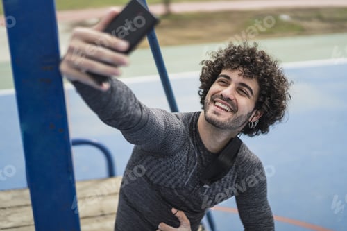 Preview: An Attractive Smiling Spanish Male With A Mask Hanging On The Ear And Taking A Selfie