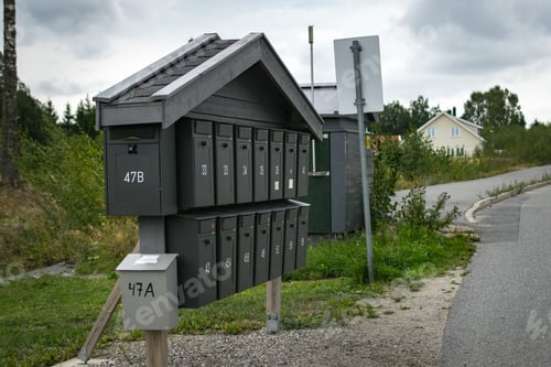 Preview: A Black Mailbox In A Street With Trees And White Houses In The Background