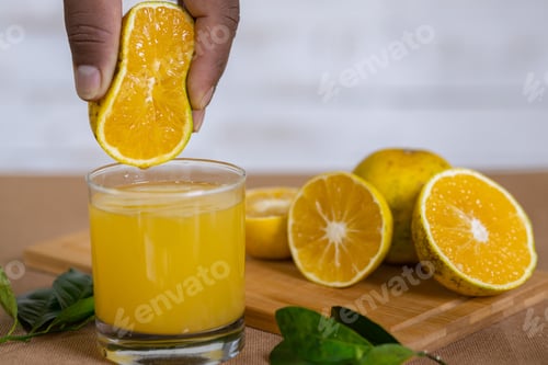 Preview: A Man Squeezing Lemon Into A Glass With Cut Lemons On A Wooden Board In The Background