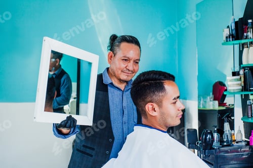 Preview: Latin Man Stylist Cutting Hair To A Client And Holding A Mirror In A Barber Shop In Mexico