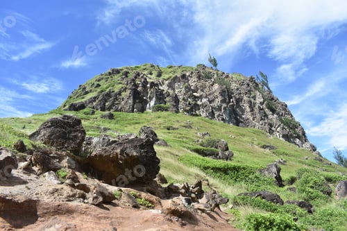 Preview: A Closeup Shot Of A Rocky Hill With Green Grass And Blue Sky On The Background