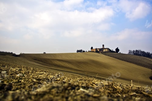 Preview: A Beautiful Shot Of A Dry Grassy Field With A House On Top Of The Hill Under A Blue Cloudy Sky