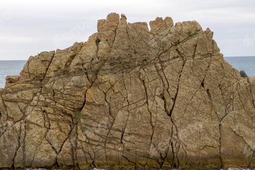 Preview: A Closeup Shot Of A Cliffy Seashore Near A Wavy Sea Under A Cloudy Sky