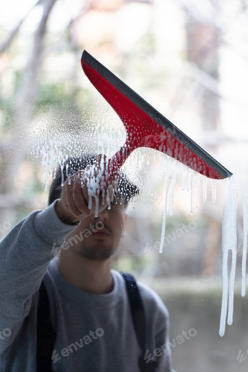 Preview: A Closeup Of A Person Cleaning Windows With A Red Squeegee Under The Lights With A Blurry Background