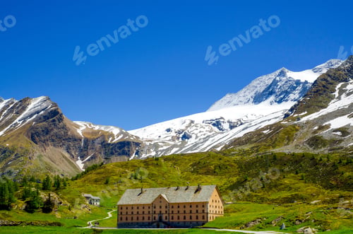 Preview: A House Surrounded By Rocky Mountains Covered In Greenery And Snow In Valais In Switzerland