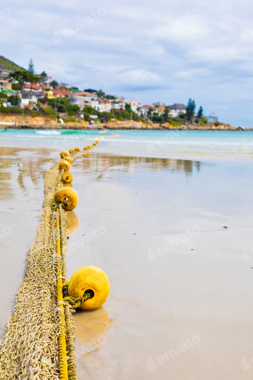 Preview: A Vertical Shot Of Buoys On A Rope Stretching From Wet Sandy Coast To The Ocean In Cape Town, South