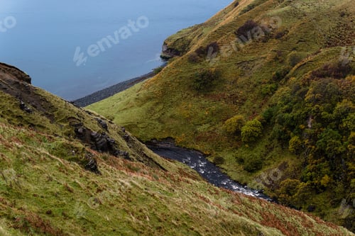 Preview: A Stunning Shot Of A Small Creek Running Through Grassy Hills And Falling Into The Sea