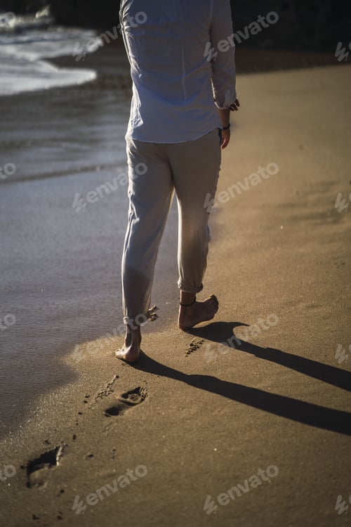 Preview: A Vertical Shot Of A Male In A White Shirt And Trousers Walking Through The Wet Sand At The Beach