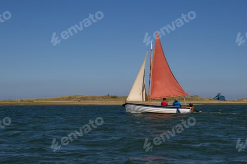 Preview: An Eye-Level Shot Of Two People Riding A Sailboat With Red And White Sails In The Sea