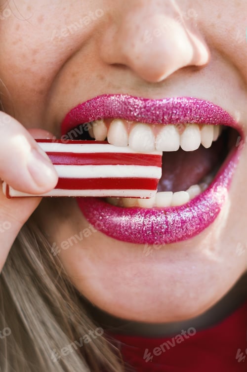 Preview: A Closeup Shot Of A Female With Freckles And A Sparkly Lipstick Taking A Bite Of A Delicious Candy