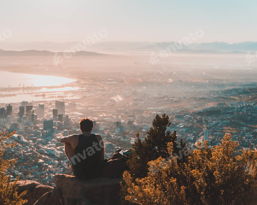 Preview: A Man Sitting On The Top Of The Rock Admiring The View Of The City Below