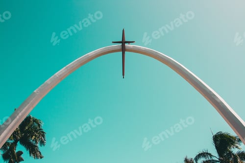 Preview: A Wide Slight Closeup Shot Of A Gateway Arch With A Cross On It Near Palm Trees Under A Clear Sky