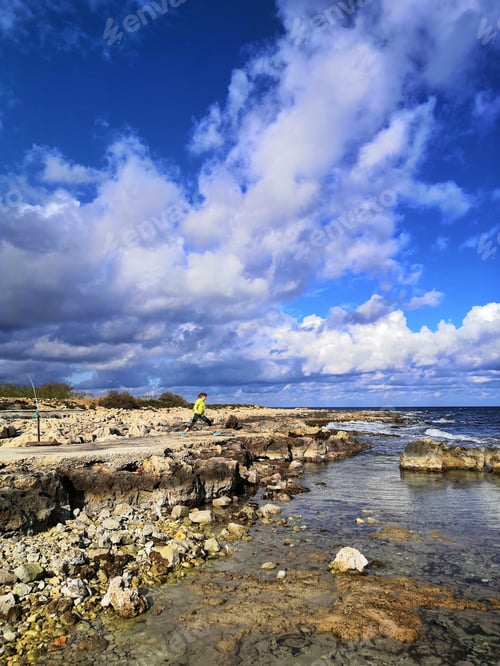 Preview: A Vertical Shot Of A Female With Yellow Jacket Stretching On The Beach By The Calm Sea On A Sunny