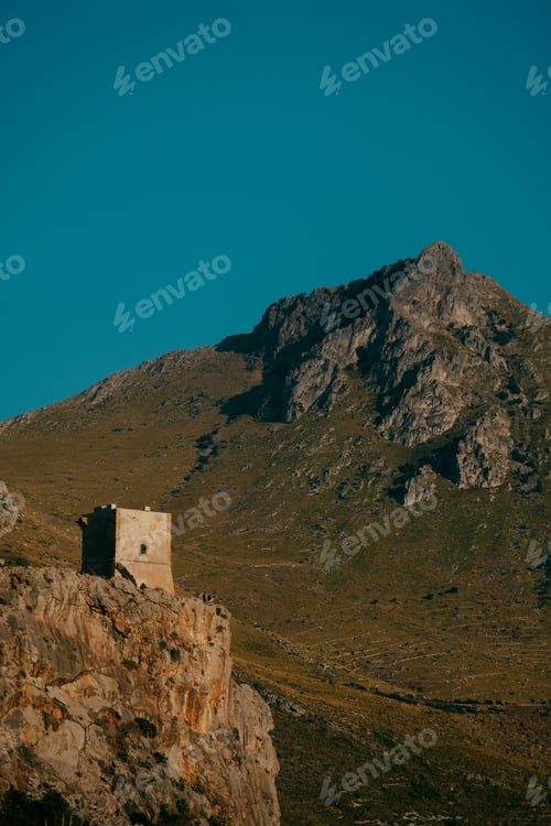 Preview: A Vertical Shot Of A House On Top Of The Cliff With A Mountain And Blue Sky In The Background
