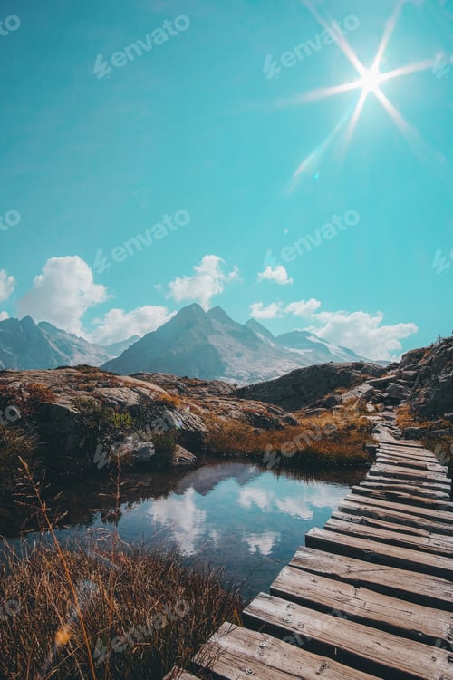 Preview: A Vertical Shot Of A Narrow Wooden Passage Over A Reflective Small Lake And A Mountain Range On The