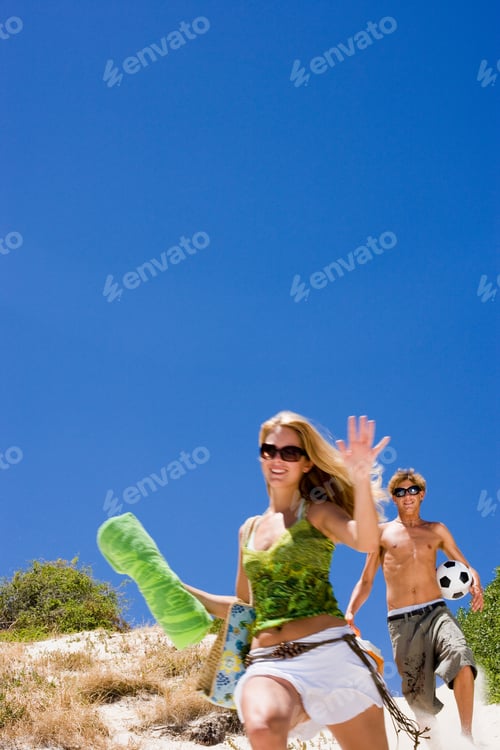 Preview: Vertical Shot Of A Teenage Couple Running Down A Sand Dune With Girl Holding Towel And Boy A Ball.