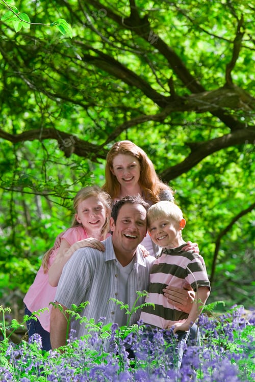 Preview: Vertical Shot Of A Happy Family Having A Picnic Near A Field Of Bluebell Flowers And Posing