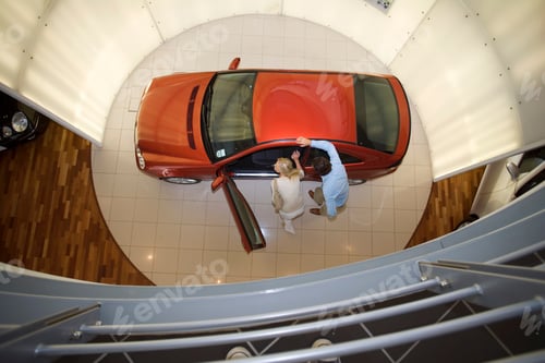 Preview: Overhead View Of A Couple Looking At A New Red Hatchback In The Car Showroom.