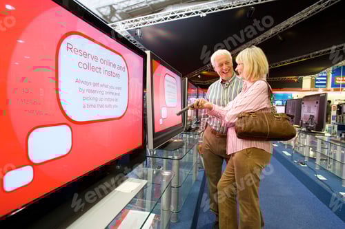 Preview: Senior Couple Standing In The Middle Of An Electronics Appliances Store And Smiling While Shopping