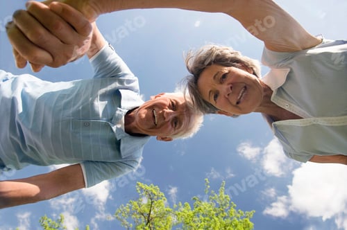 Preview: Senior Couple Holding Hands And Looking Down At The Camera On A Beautiful Spring Day In The Field.