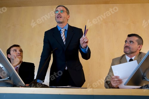 Preview: Portrait Of A Businessman In Center Delivering Speech And Gesturing As Colleagues By His Side