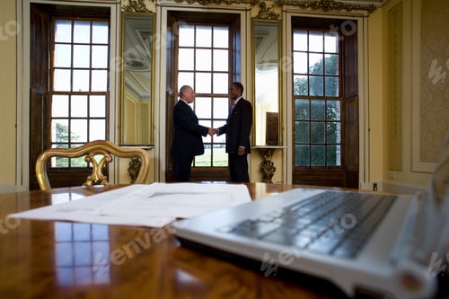 Preview: Two Senior Businessmen Shaking Hands In The Background With An Open Laptop And Some Paperwork Lying