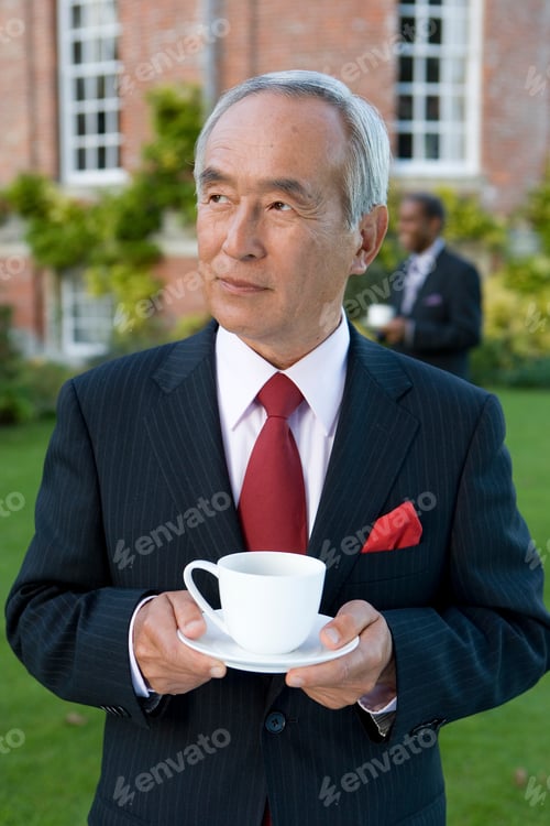 Preview: Senior Businessman Standing In The Lawn With A Cup Of Tea In His Hands In Front Of His Manor House
