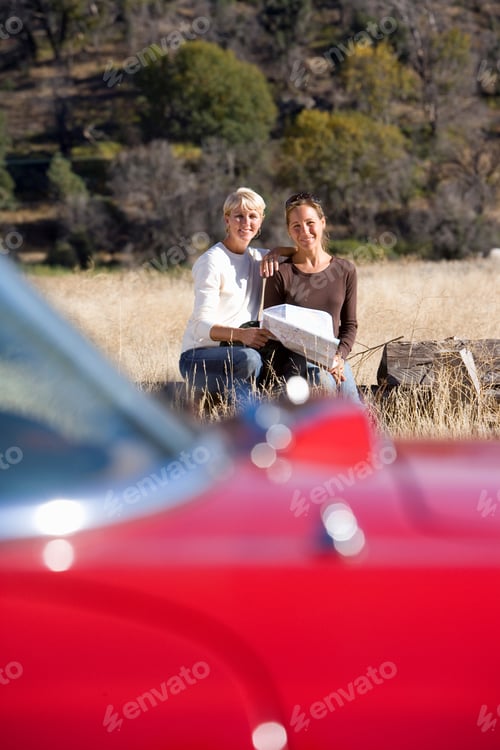 Preview: Vertical Shot Of A Mother And Daughter Sitting On A Log With A Map Behind Their Car In A Remote