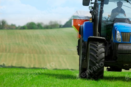 Preview: Man Driving A Blue Colored Tractor Spreading Fertilizer In His Field On A Bright Sunny Day With