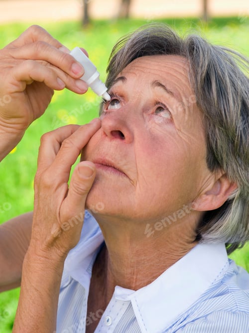 Preview: Senior Woman Wearing A Blue Shirt Using Eye Drops Out In The Field