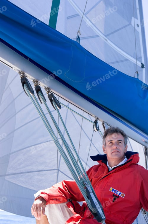 Preview: Close-Up Shot Of A Mature Man In A Red Jacket Sitting On The Deck Of The Sailing Boat Below Sail.