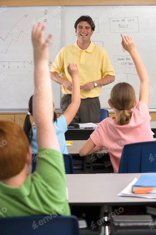 Preview: Vertical Shot Of Smiling Male Teacher Standing By A Whiteboard In A Classroom Looking At The