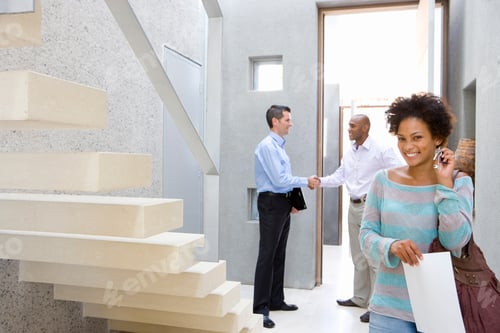 Preview: Middle-Aged Woman Holding House Keys Next To A Flight Of Stairs And Smiling With Her Husband