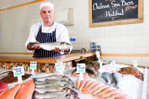 Preview: Horizontal Shot Of A Middle-Aged Fishmonger Standing Behind The Counter In The Shop And Holding Up