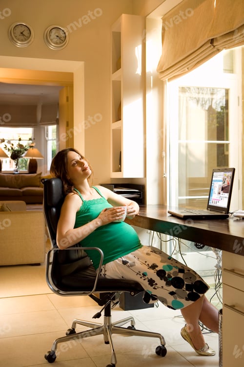 Preview: Young Pregnant Woman Sitting On The Chair Next To Her Desk In The Home Office And Smiling