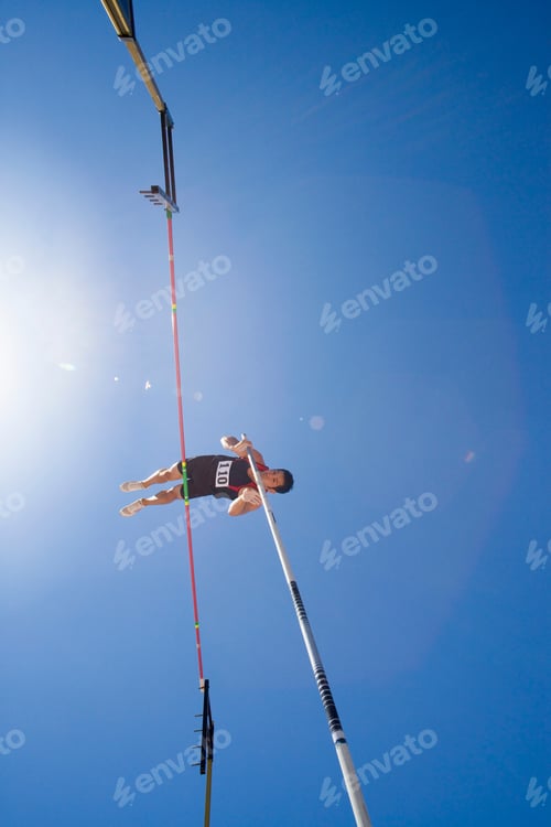 Preview: Low Angle View Of A Pole Vault Athlete Going Over Bar With A Clear Blue Sky And Lens Flare In The