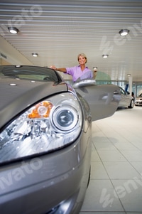 Preview: Front View Portrait Of A Senior Woman Looking At A New Silver Convertible Car In The Large Showroom.