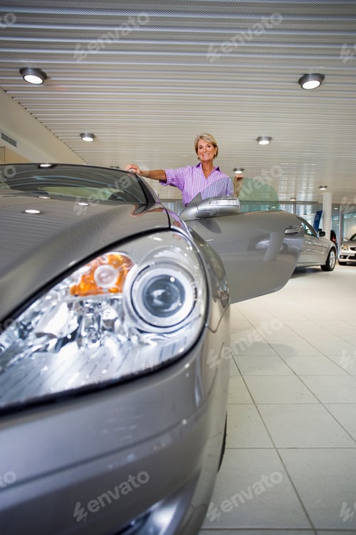 Preview: Front View Portrait Of A Senior Woman Looking At A New Silver Convertible Car In The Large Showroom.