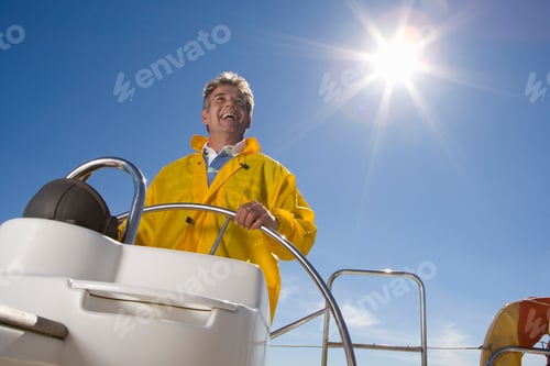 Preview: Low Angle Waist Up Shot Of A Happy Senior Man Steering A Boat On A Clear Day With A Sun Flare In