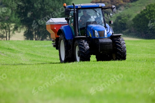 Preview: Front View Of A Man Driving A Blue Colored Tractor In His Field Spreading Fertilizer On A Bright