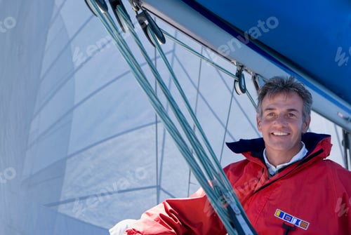 Preview: Low Angle View Of A Mature Man In A Red Jacket Sitting On The Deck Of The Sailing Boat Below Sail.