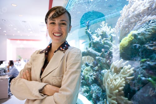 Preview: Horizontal Waist Up Portrait Of A Smiling Young Businesswoman With Crossed Arms By The Fish Tank In
