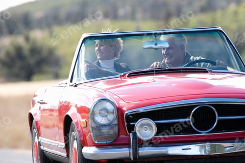 Preview: Horizontal Front View Of A Joyous Senior Couple On Road Trip In A Red Convertible With Man Pointing