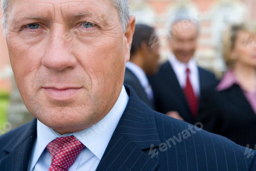 Preview: Headshot Of A Senior Businessman Looking Confidently At The Camera With His Colleagues Standing And