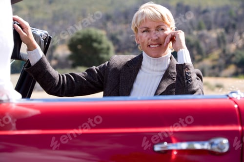 Preview: Horizontal Profile Shot Of A Seated Senior Woman Posing Inside A Red Convertible On A Sunny Day
