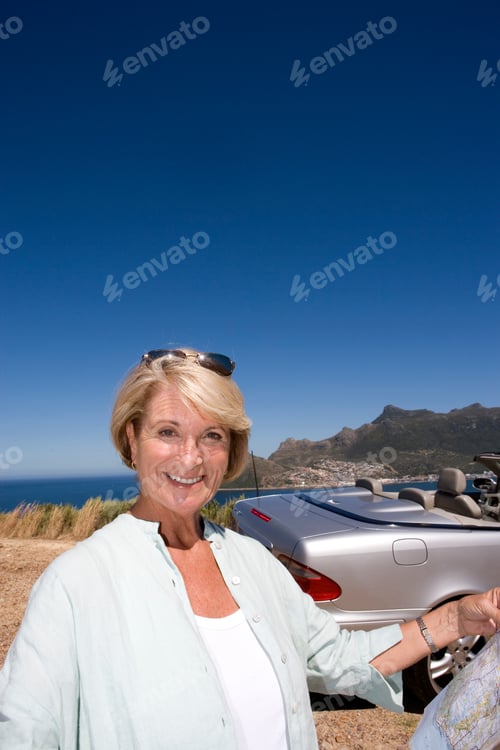 Preview: Senior Woman Standing In Front Of A Car And Smiling At Camera While Holding A Map In Her Hand