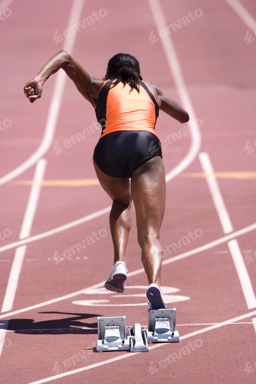 Preview: Rear View Of An African Female Runner Setting Off From Her Starting Blocks At The Race Start At An