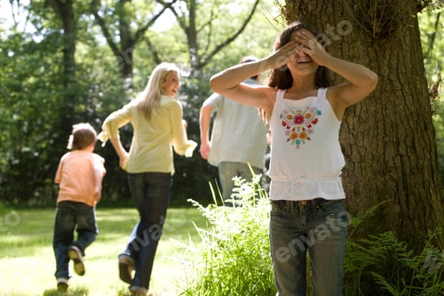Vista previa: Horizontal Shot Of A Family Of Four Playing Hide And Seek In The Forest With The Girl Covering Eyes